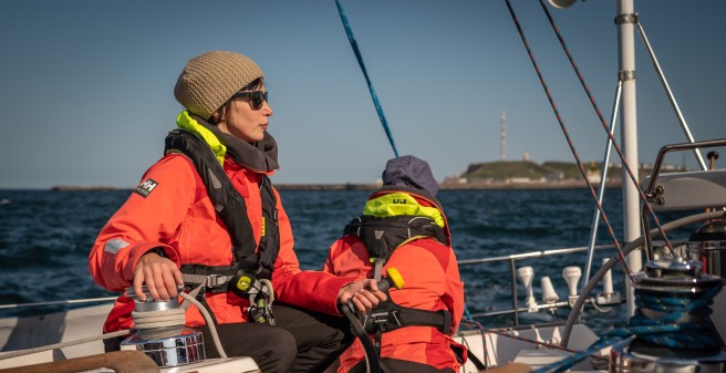 Segelrebellen, eine Frau in roter Jacke und Mütze schaut konzentriert auf den Horizont