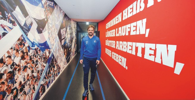 Daniel Petrowski geht durch einen schmalen Gang auf den Fotografen zu. An der Wand Bilder jubelnder Fans und folgender Text: Gewinnen heißt: Länger laufen, Härter arbeiten, Mehr geben.